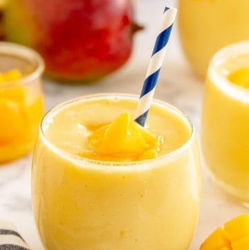 A mango smoothie in a small glass with a blue and white straw.