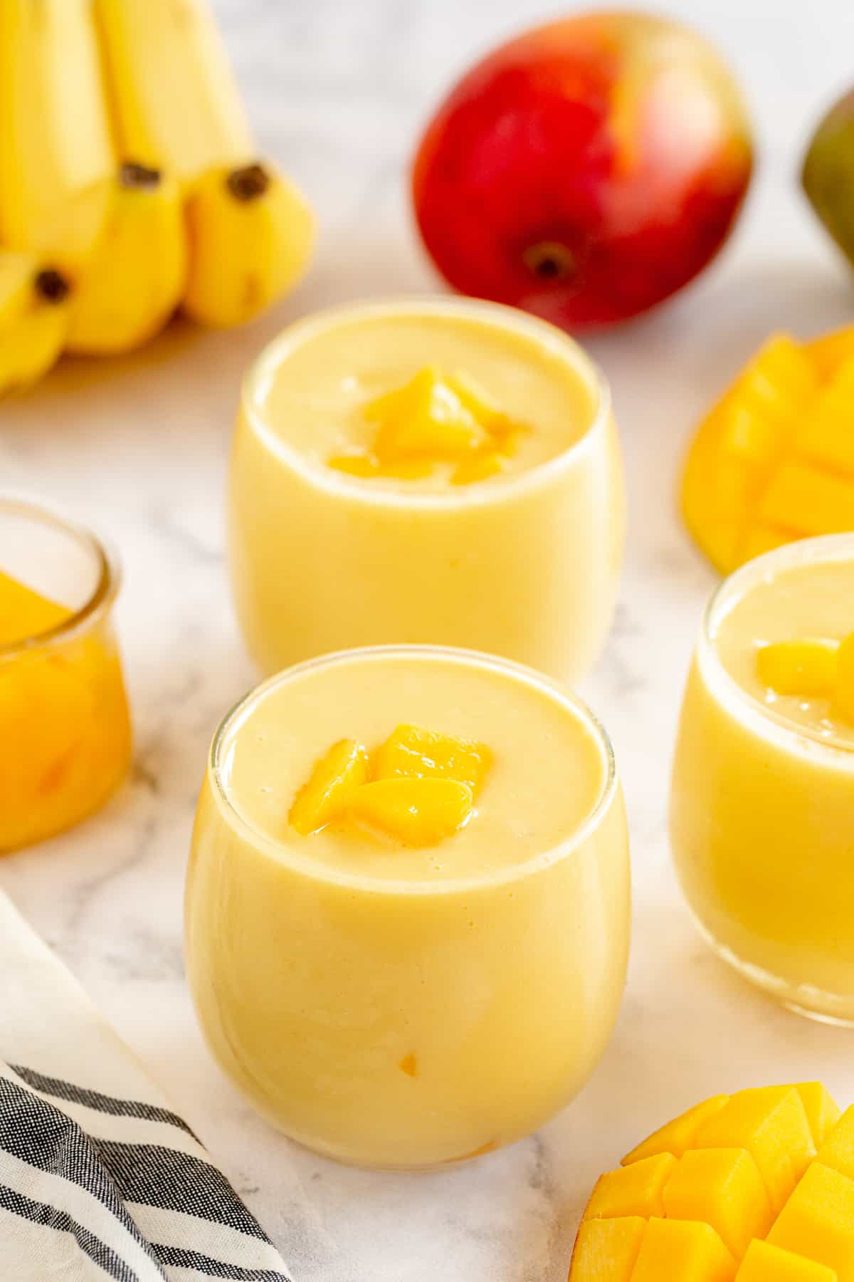 Two mango smoothies with honey, bananas, and a mango in the background.