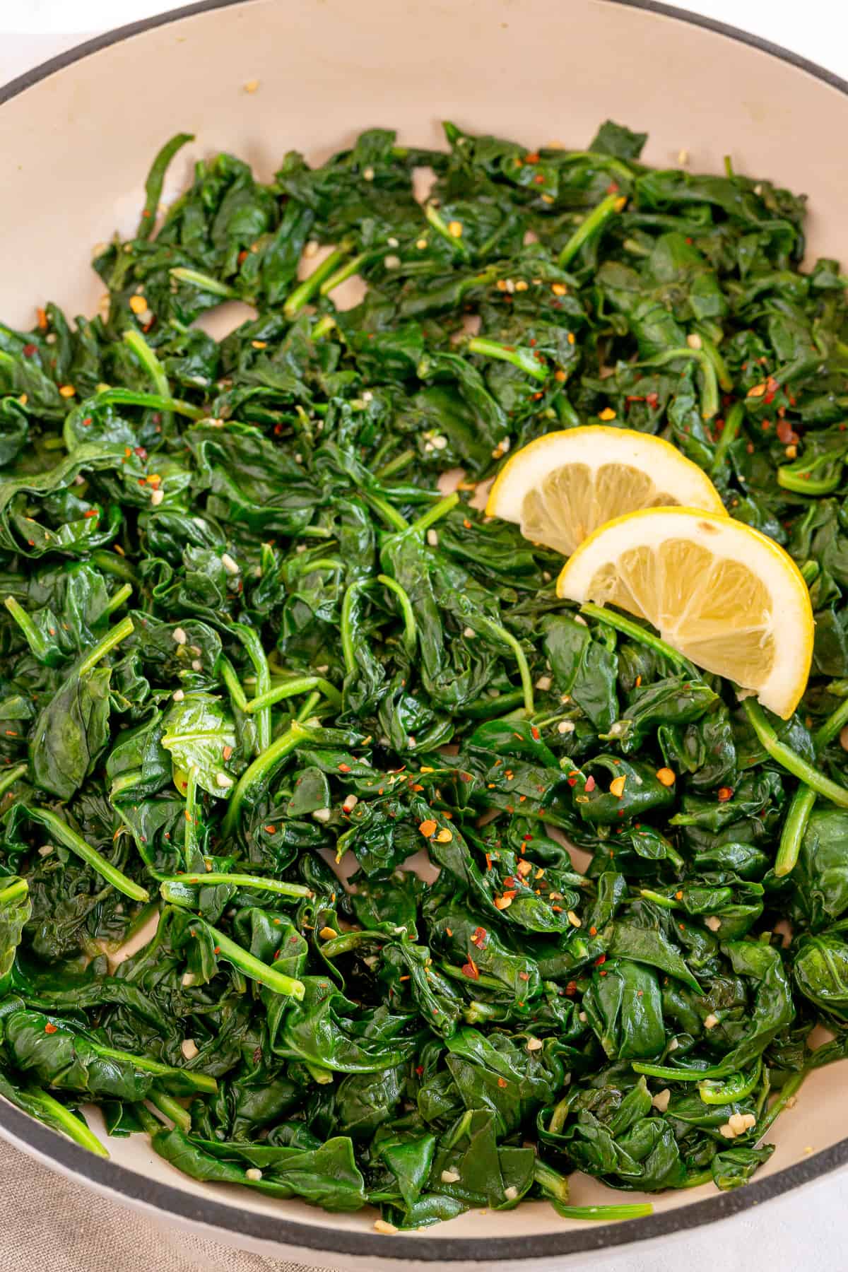 Sautéed spinach in a pan with lemon wedges.