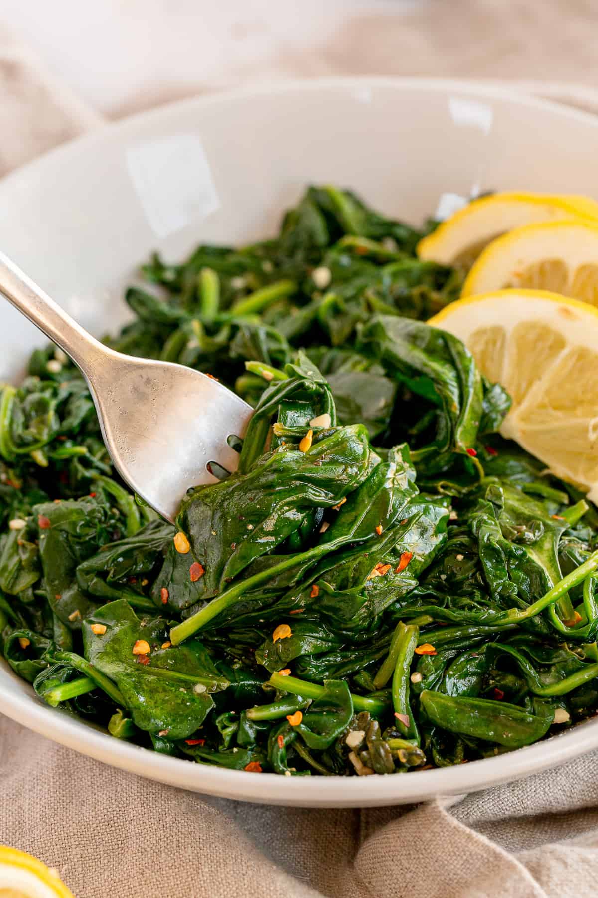 A fork presses down into a bowl of cooked spinach.