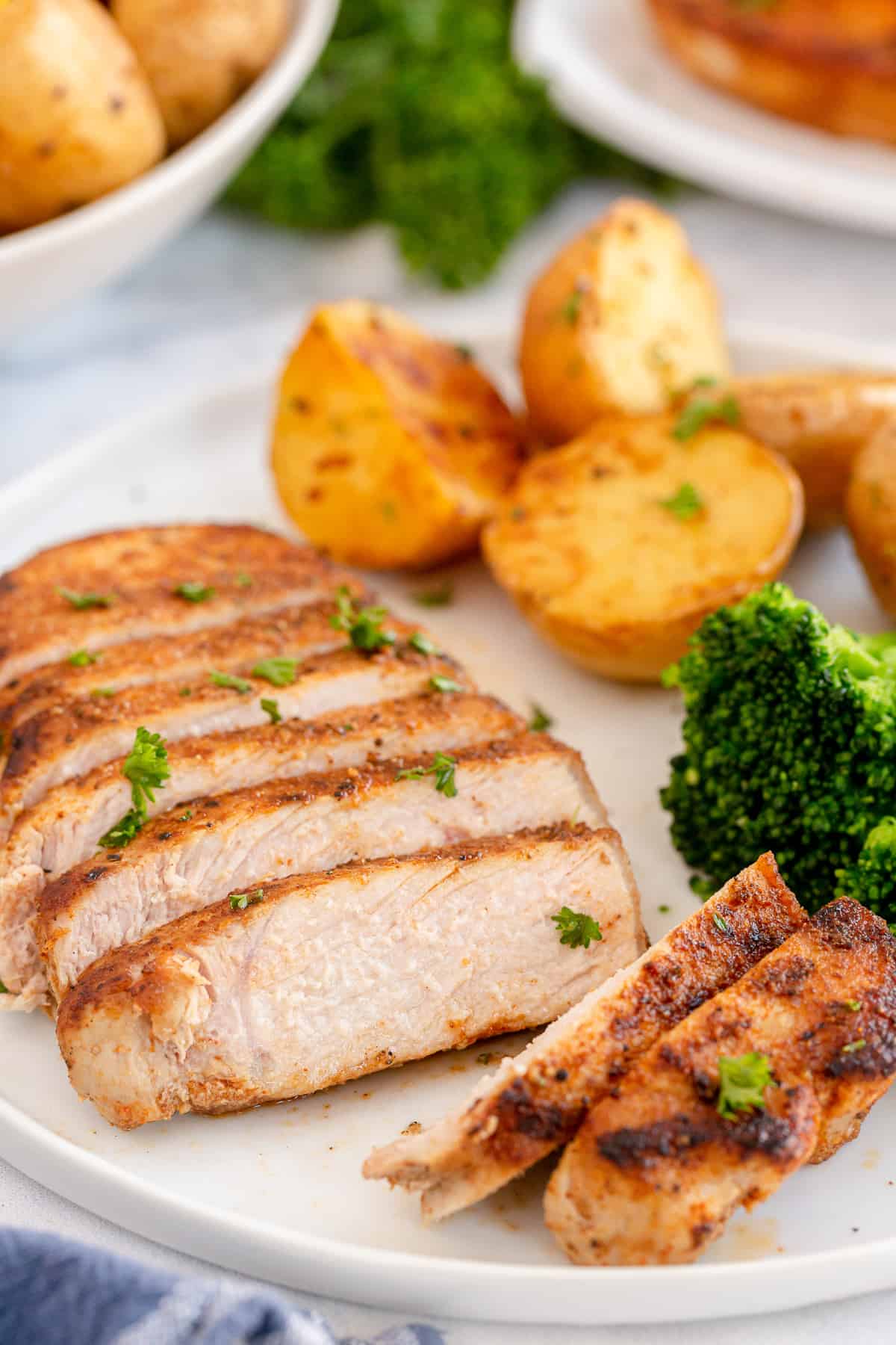 A sliced boneless pork chop on a plate with broccoli and potatoes.