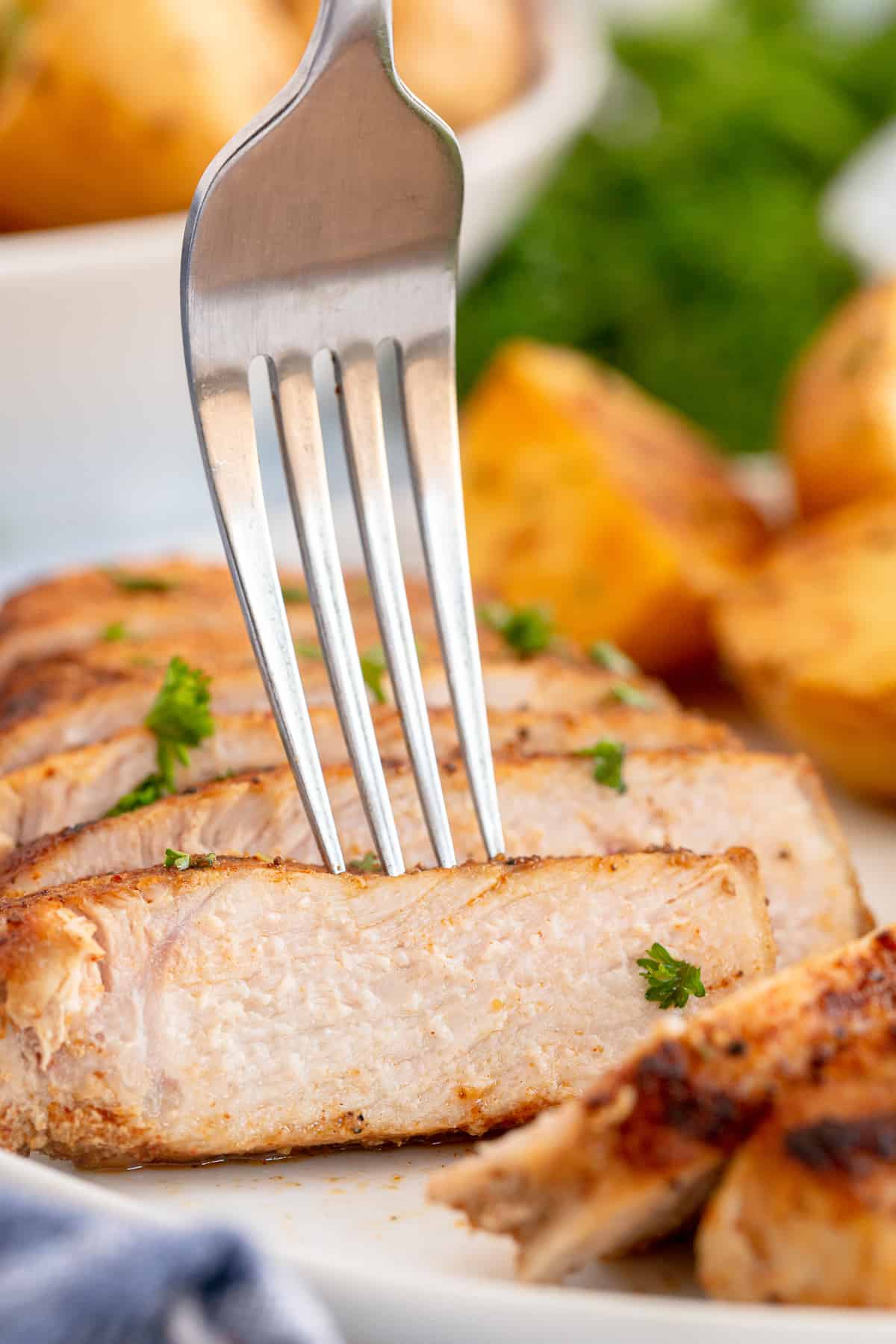 A fork pressing into a slice of pork chop on a dinner plate.