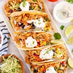 An over the top shot of a platter of chicken tacos with toppings.