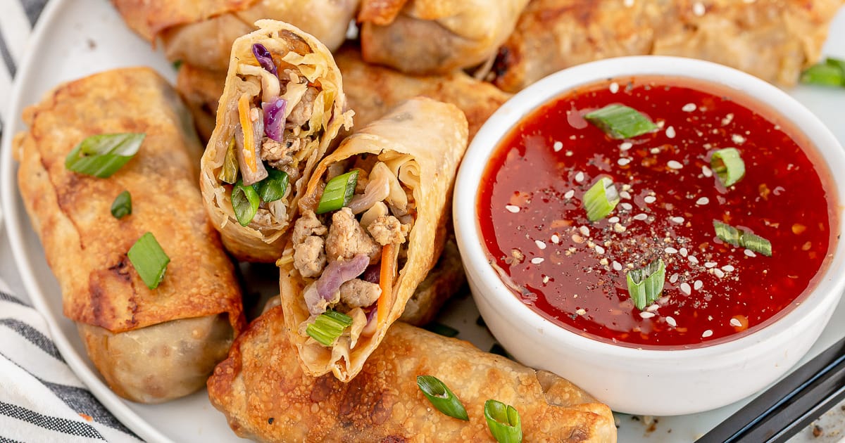 An egg roll sliced in half on a platter with a bowl of red sweet chili sauce.