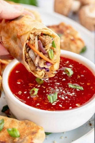 An egg roll that has been sliced in half dipping into sweet chili sauce.