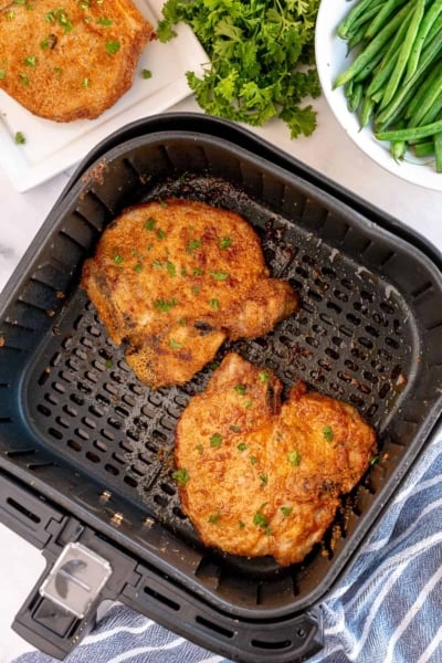 Two cooked pork chops in an air fryer.