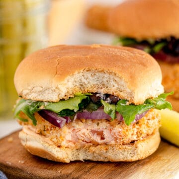 A breaded salmon sandwich with red onion and lettuce with a bite missing.