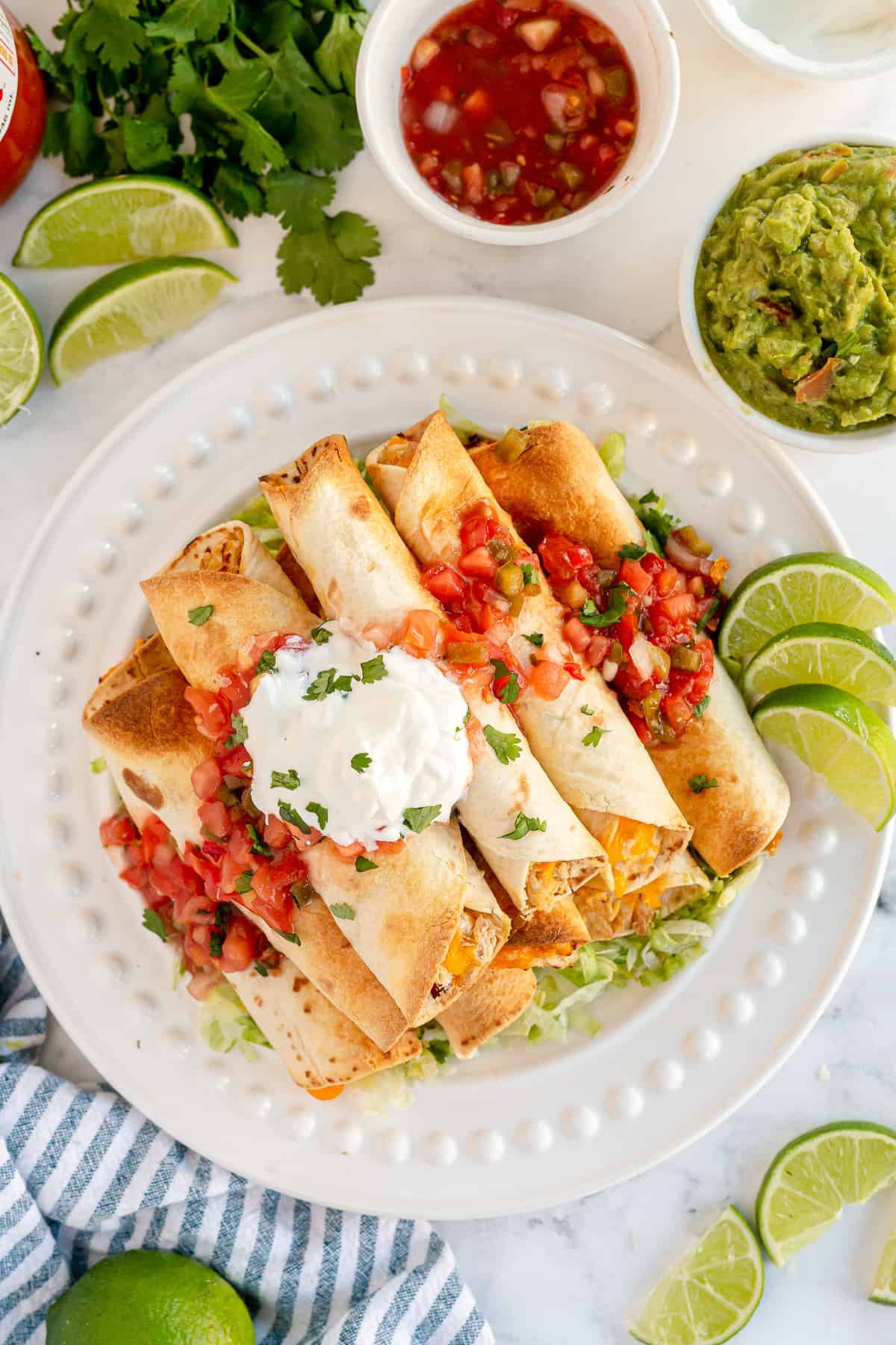 A pile of taquitos on a plate with salsa and sour cream.
