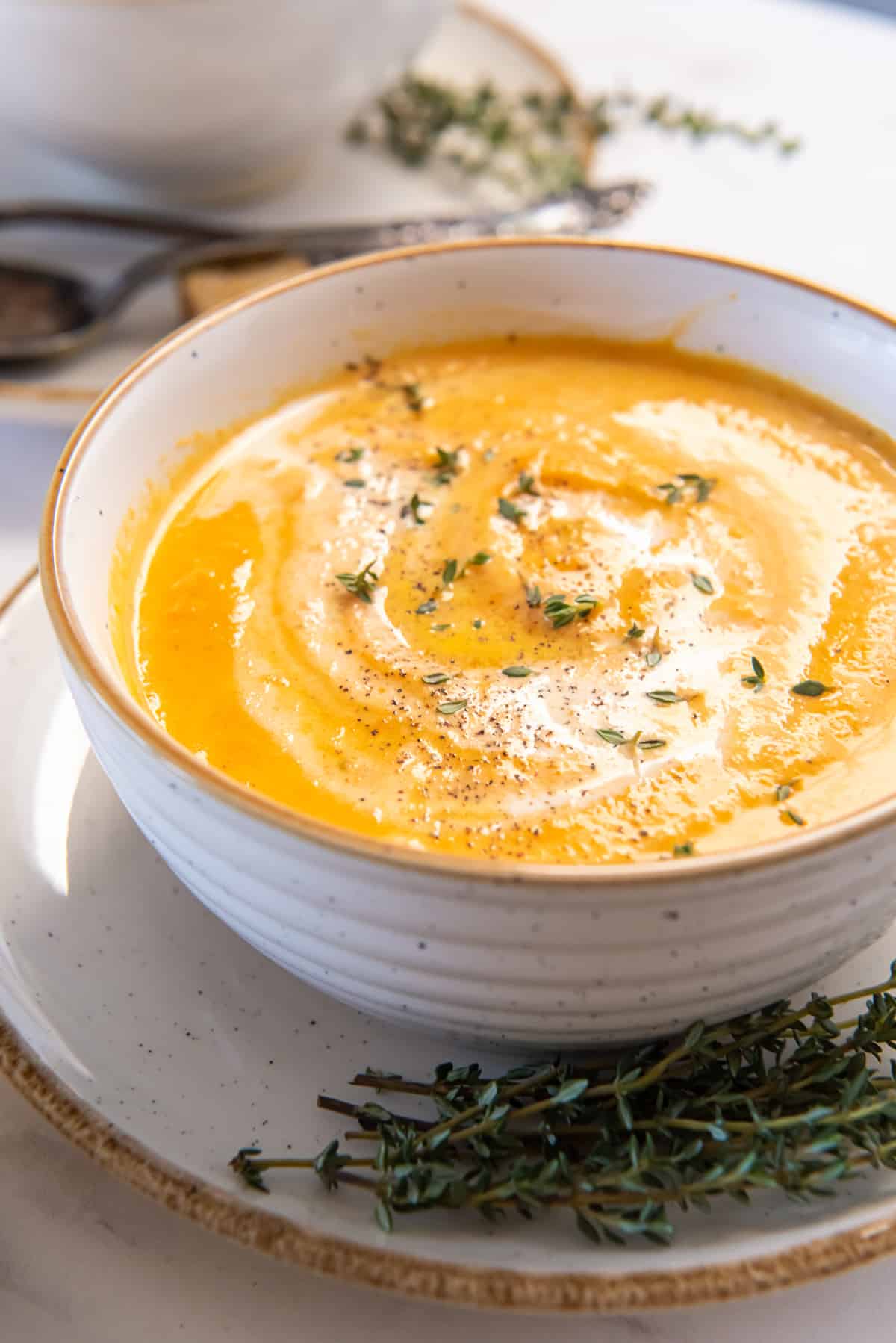 Carrot Soup in a white bowl with sprigs of fresh thyme.