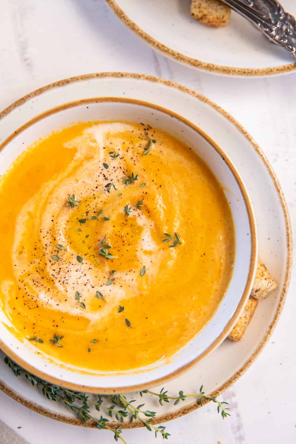 A top down shot of Carrot Soup in a white bowl.