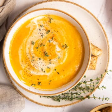 A top down shot of Carrot Soup in a white bowl with fresh thyme.