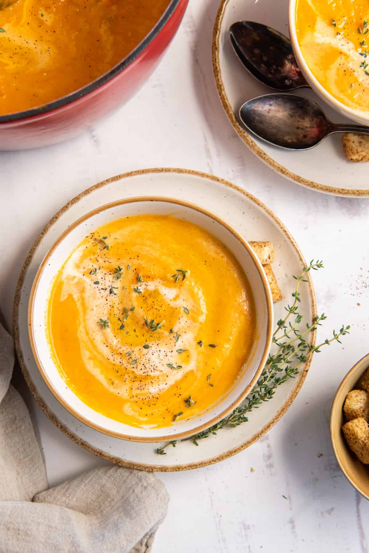 A top down shot of a bowl of carrot soup topped with cream and thyme.