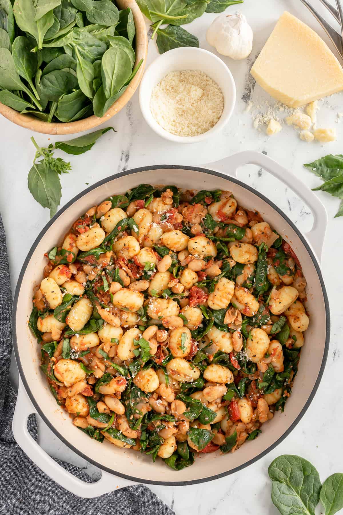 A pot of gnocchi with white beans next to spinach and parmesan.