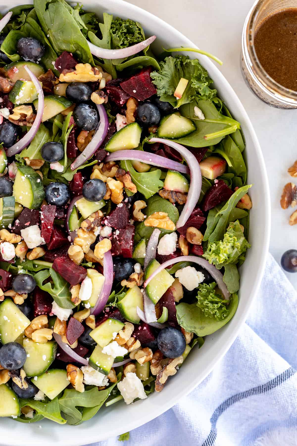  A top down shot of a green salad with blueberries beets feta and red onions.