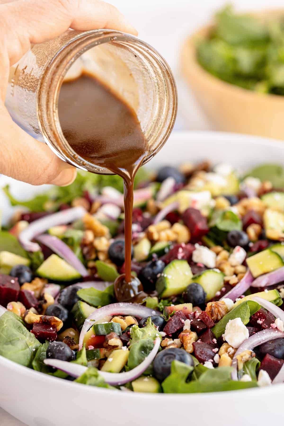 Balsamic dressing pouring on to a salad in a white bowl.