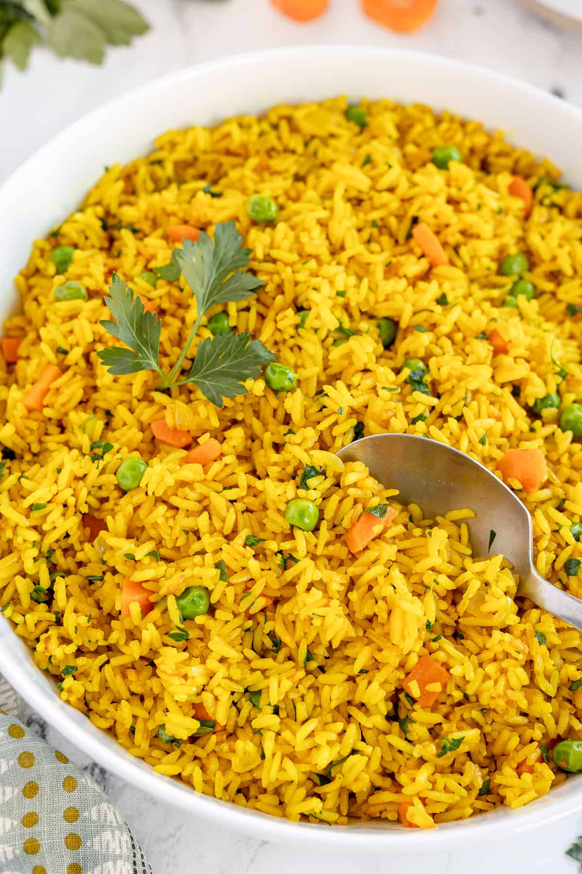 A spoon resting in a bowl of Yellow Rice with carrots and peas.