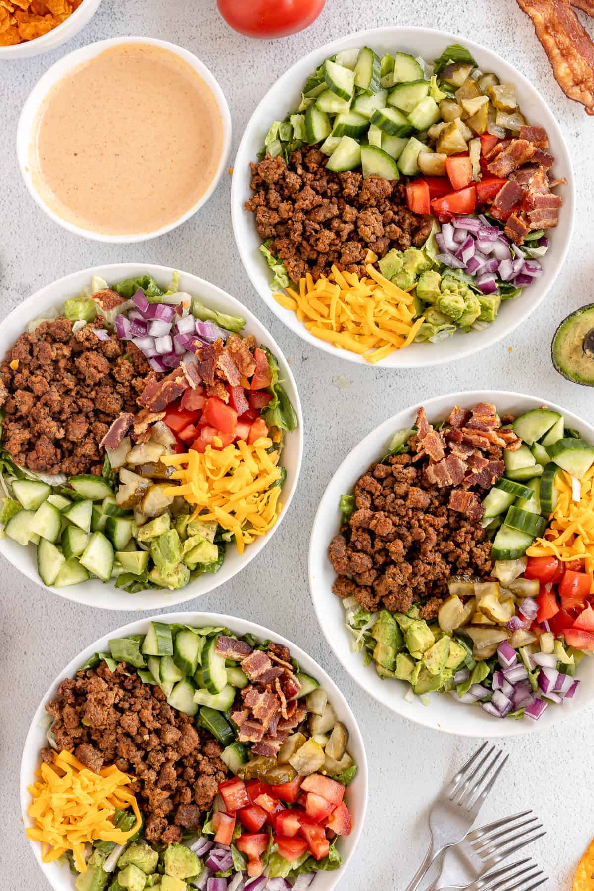 A top down shot of cheeseburger ingredients in bowls next to a small bowl of dressing.