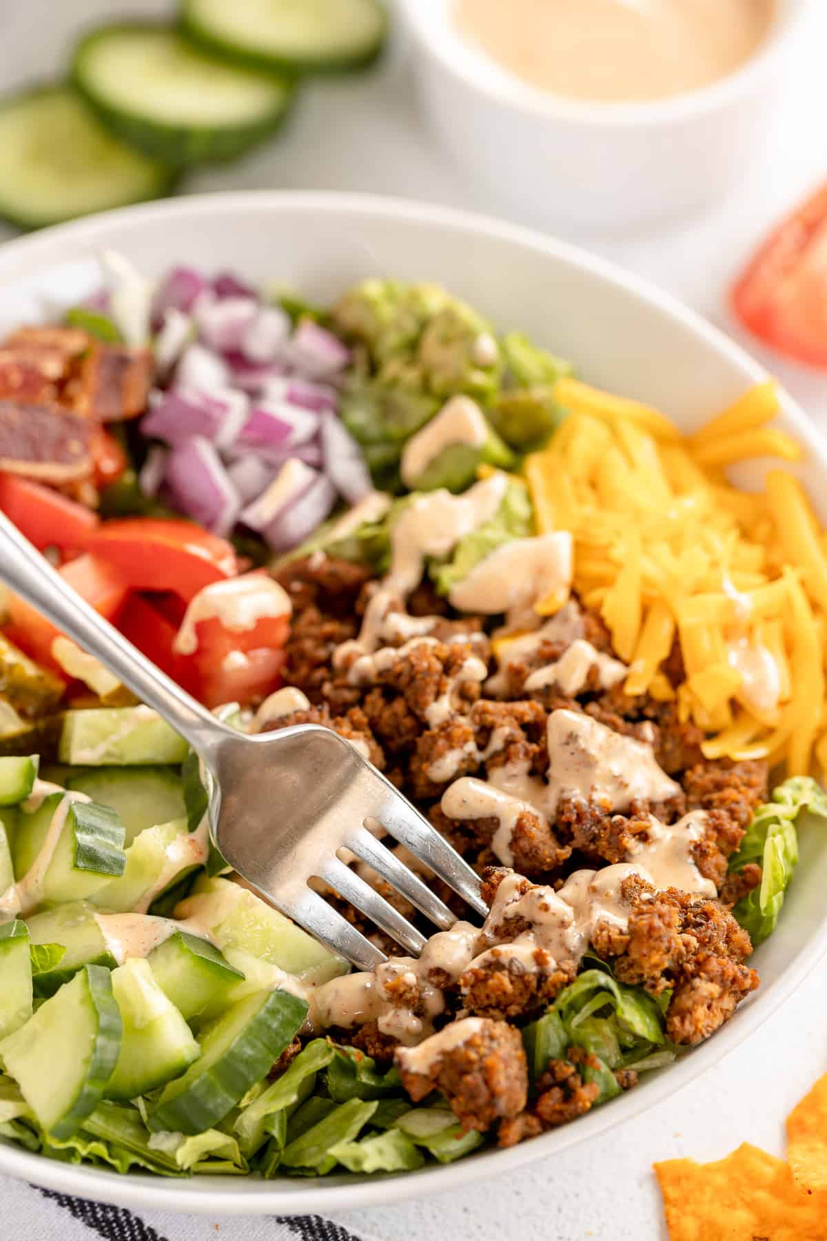 A fork pressing into ground beef in a bowl with other ingredients.
