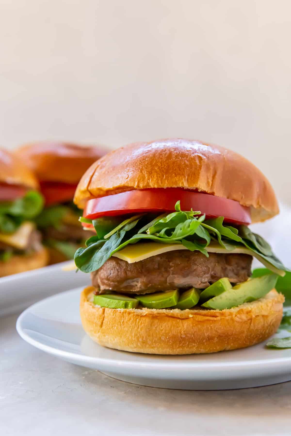 A turkey burger with tomato, spinach, and avocado on a white plate.