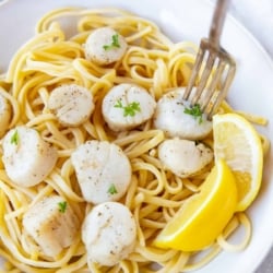 A fork piercing a scallop in a bowl with pasta and lemon.