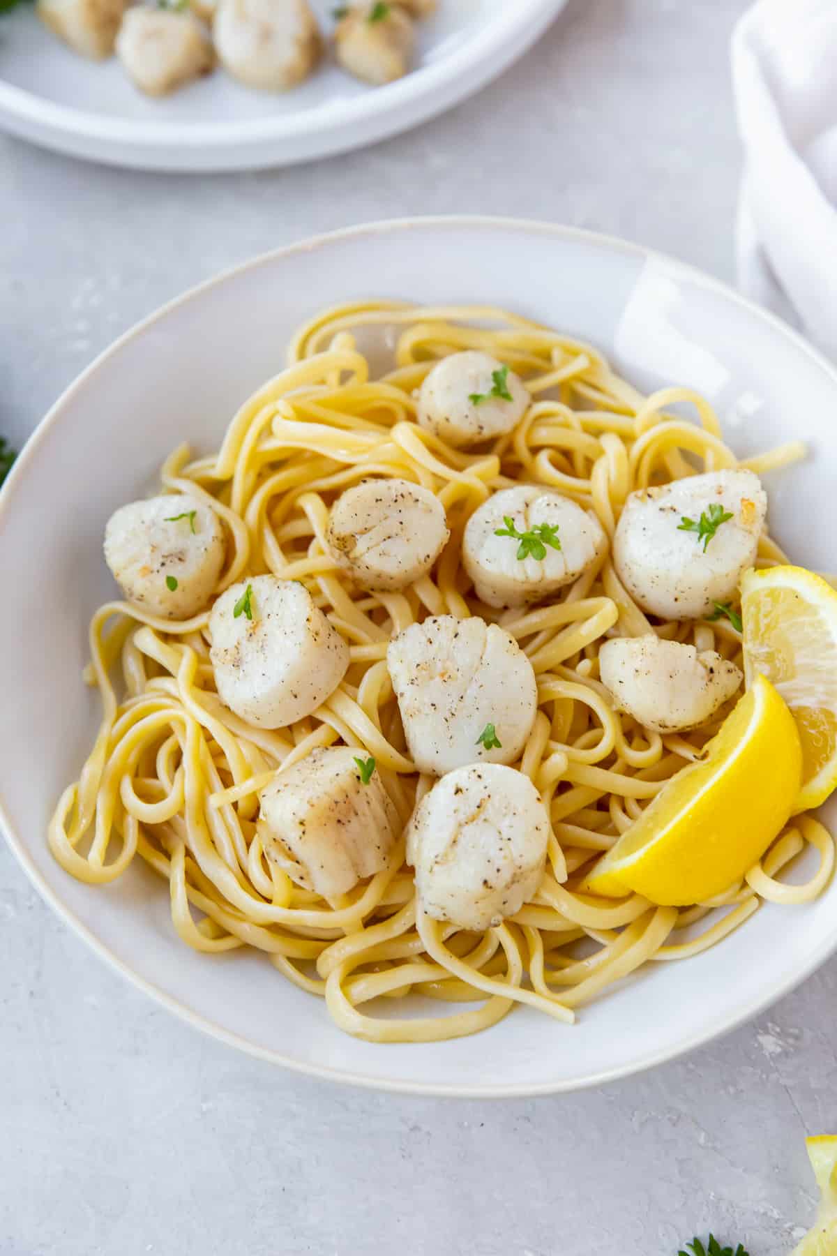 Scallops over pasta in a bowl with lemon wedges.