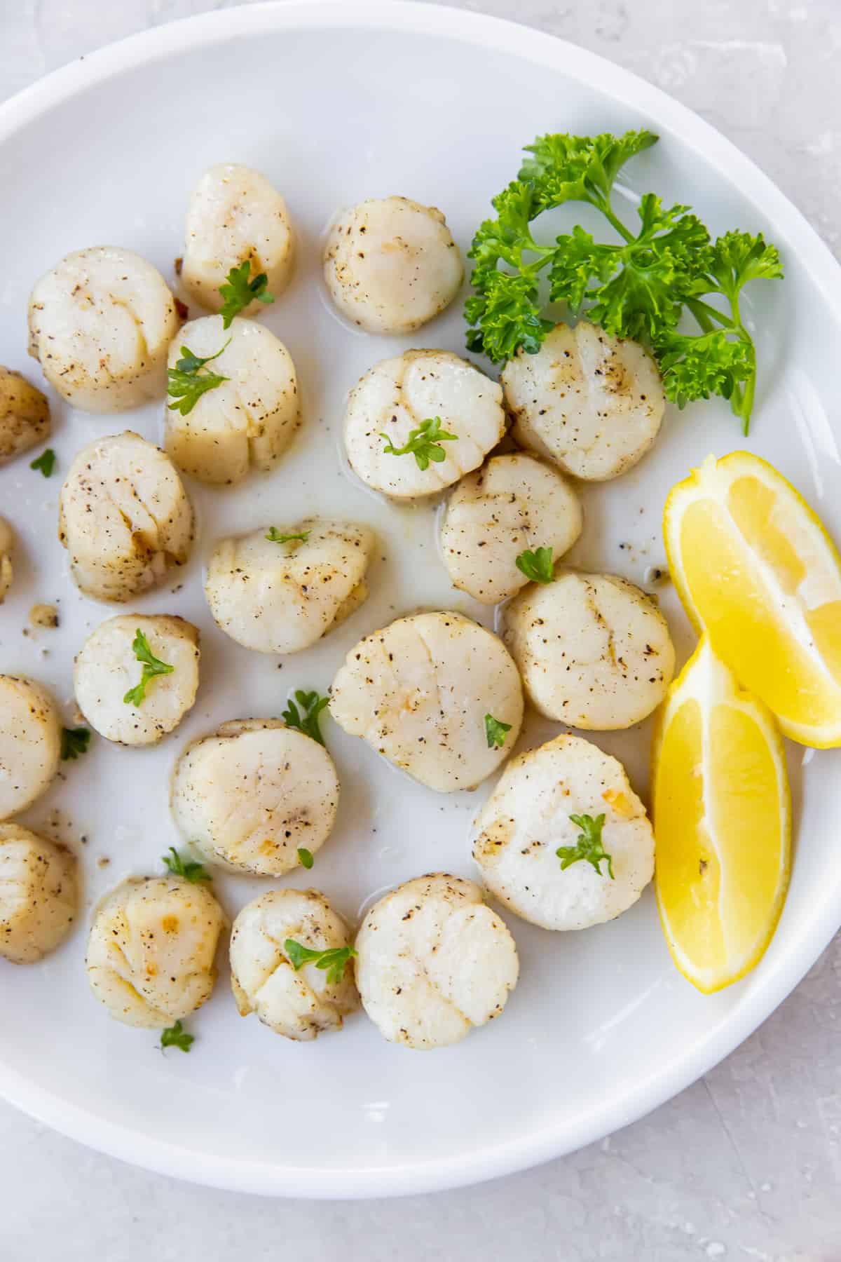 A top down shot of scallops on a plate with parsley and lemon.