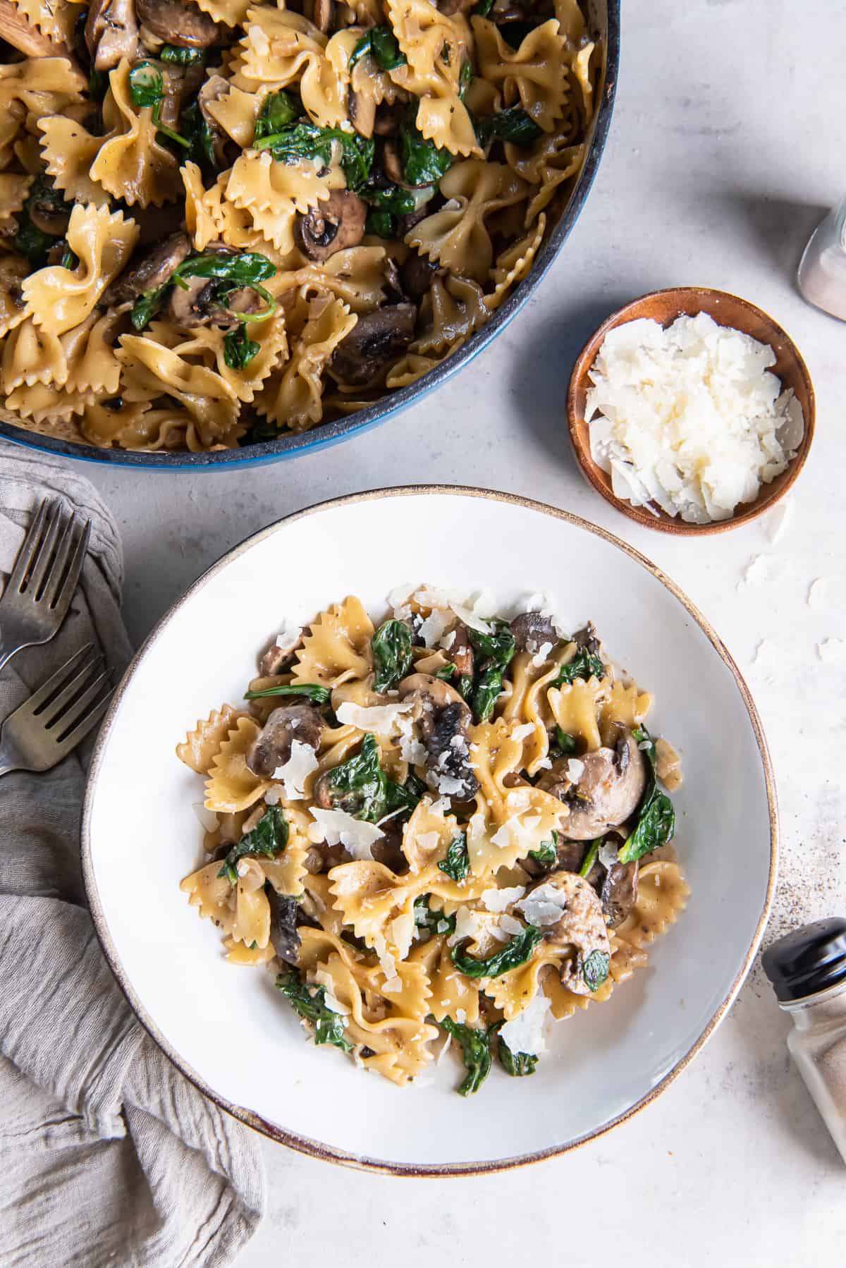 A blue skillet and white bowl filled with mushroom spinach pasta.