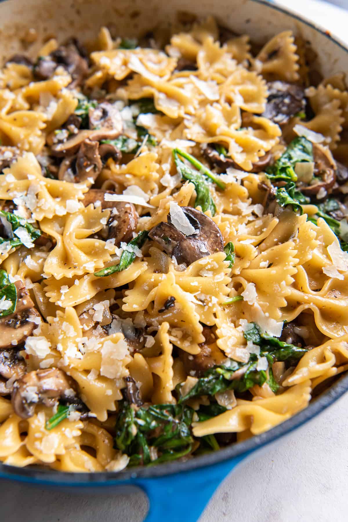 Bowtie pasta with mushrooms and spinach in a blue skillet.