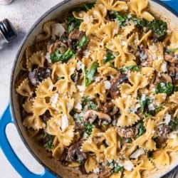 A top down shot of pasta with mushrooms and spinach in a skillet.