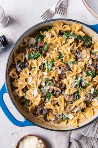 A top down shot of pasta with mushrooms and spinach in a skillet.