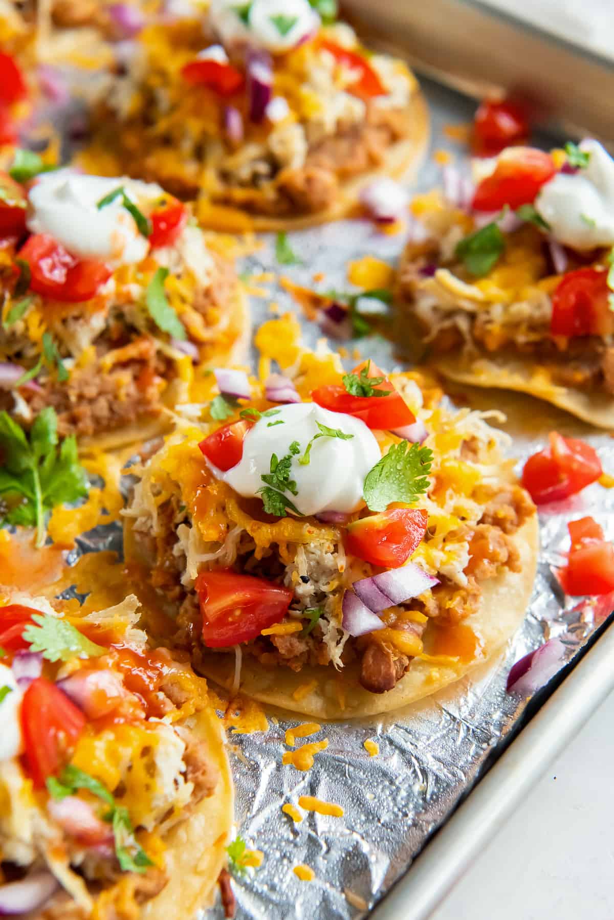 Mini tostadas with sour cream and tomatoes on a baking sheet shot from the side.