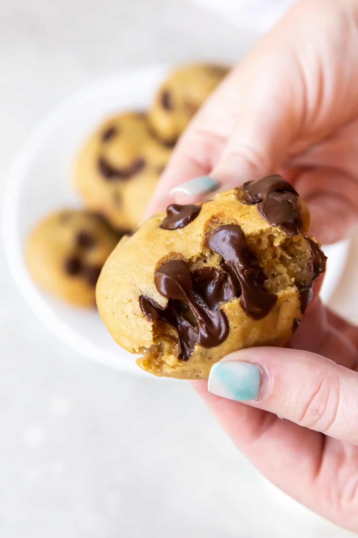 Hands breaking a chocolate chip cookie in half to reveal melted chocolate chips.