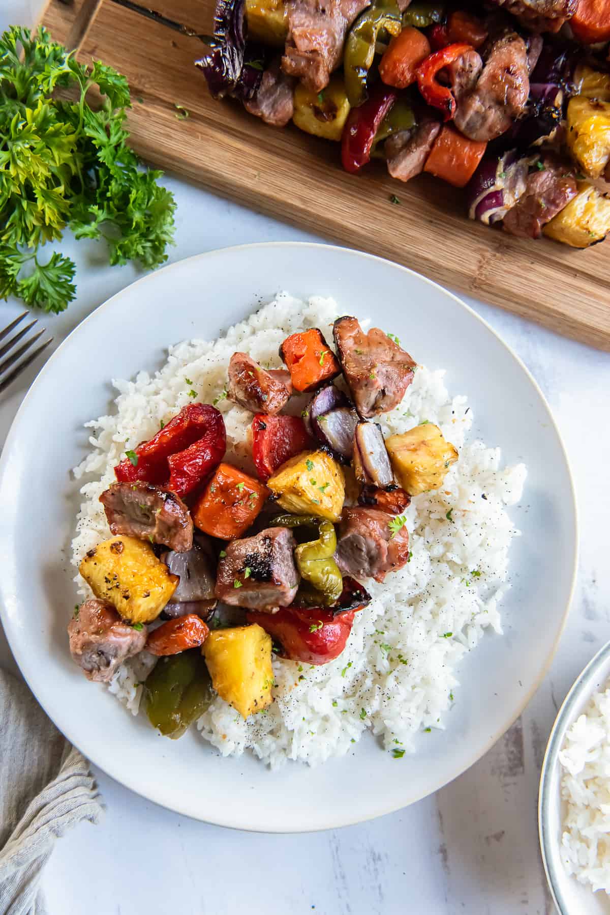 Pork, pineapple, and vegetables off the skewer and on a bed of white rice on a plate.