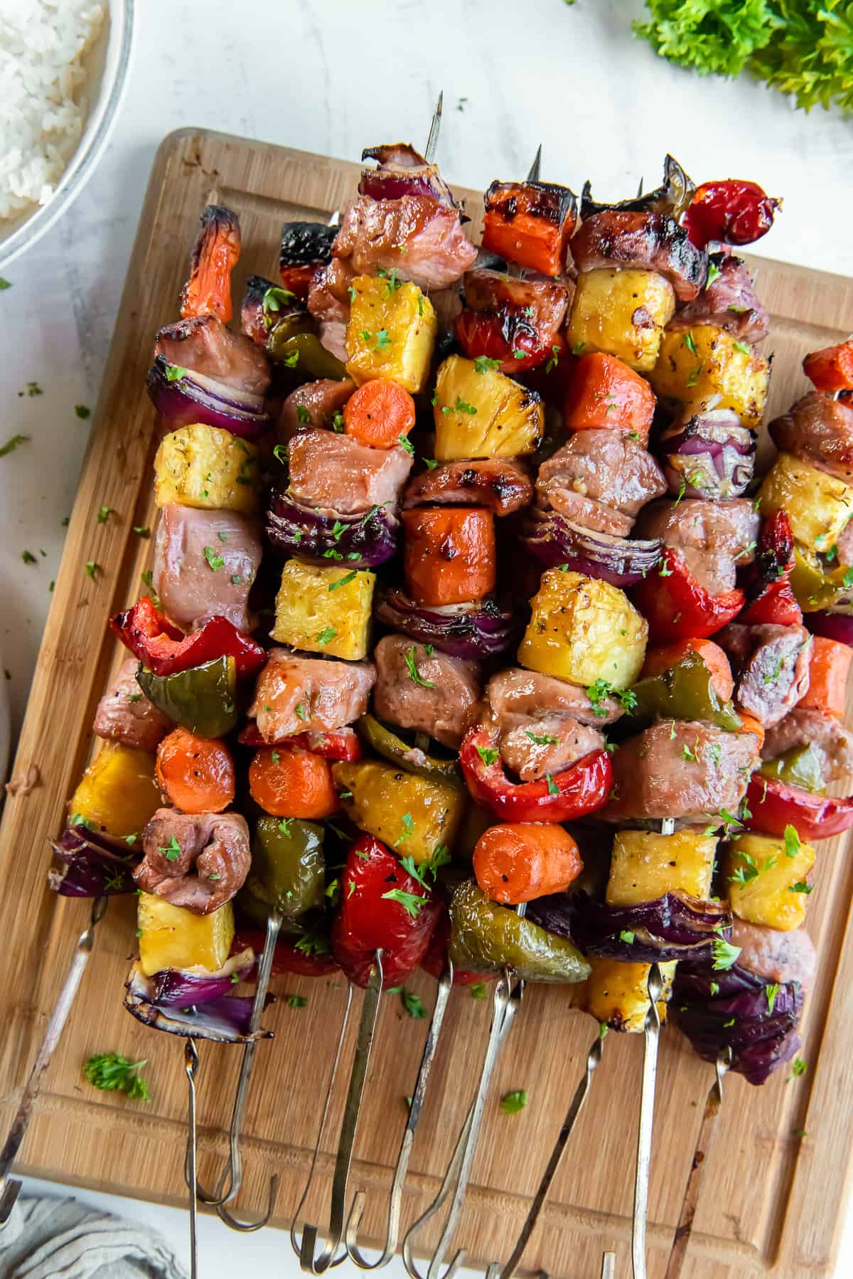 Pork Kabobs with pineapple, carrots, bell peppers, and onion piled on a wood cutting board.