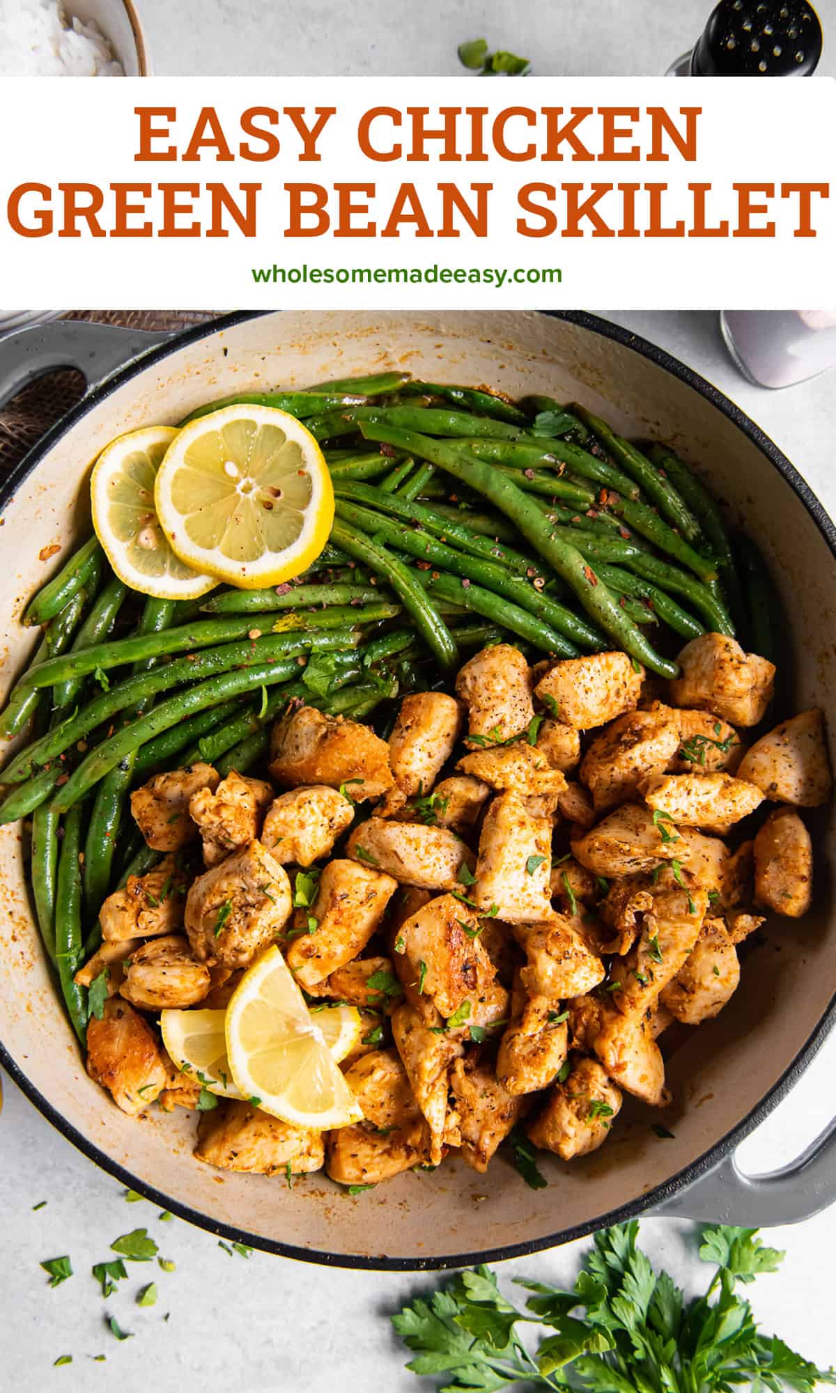 A top down shot of cooked chicken chunks and green beans in a skillet with lemon slices with text.