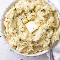 A spoon resting in a bowl of mashed potatoes topped with a pat of butter.