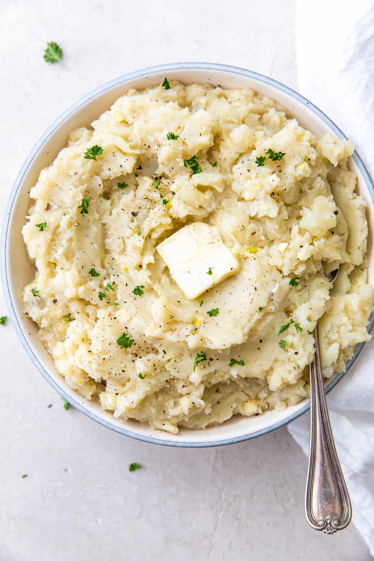 A spoon resting in a bowl of mashed potatoes topped with a pat of butter.