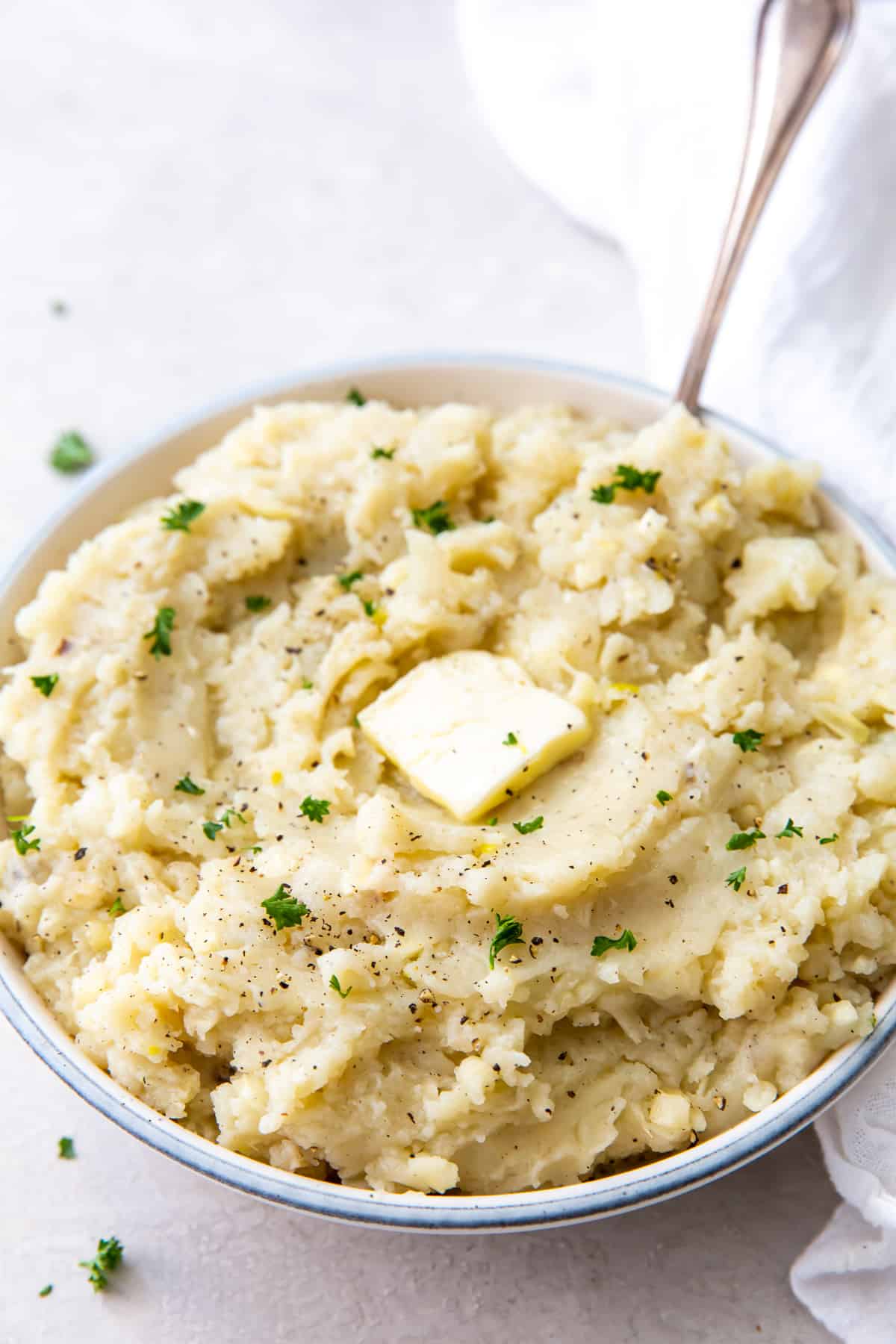  A spoon resting in a bowl of mashed potatoes topped with a pat of butter.