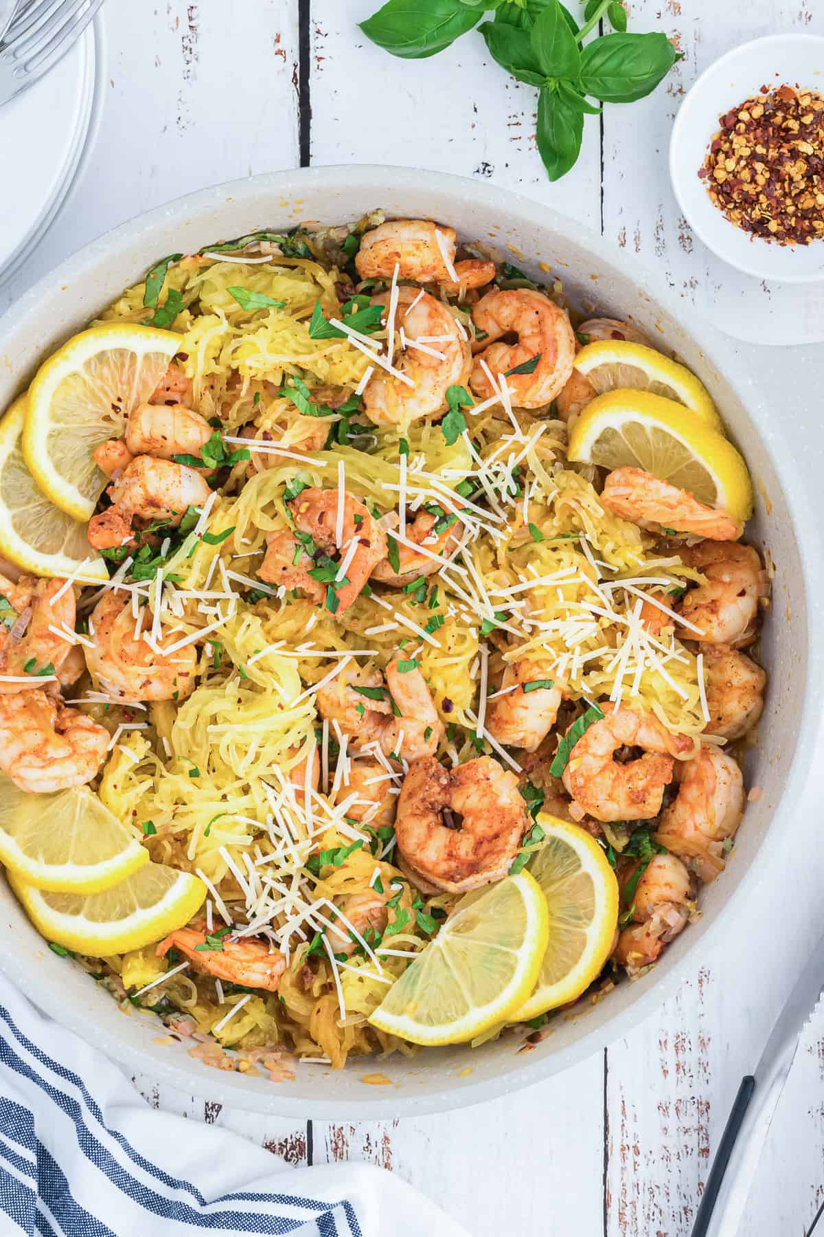 A top down shot of shrimp in a skillet with spaghetti squash, lemons, basil, and Parmesan.