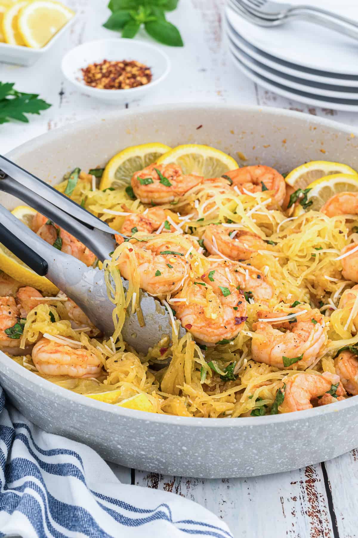 Tongs lift shrimp scampi with spaghetti squash from a skillet.