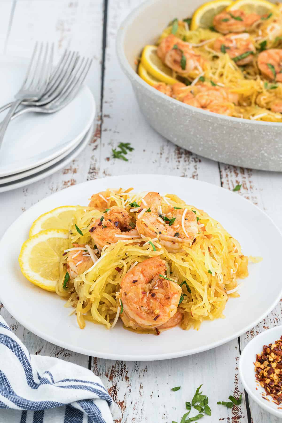 Spaghetti squash shrimp scampi on a white plate in front of a skillet full of the recipe.