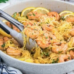 Metal tongs scooping up spaghetti squash shrimp scampi from a skillet.