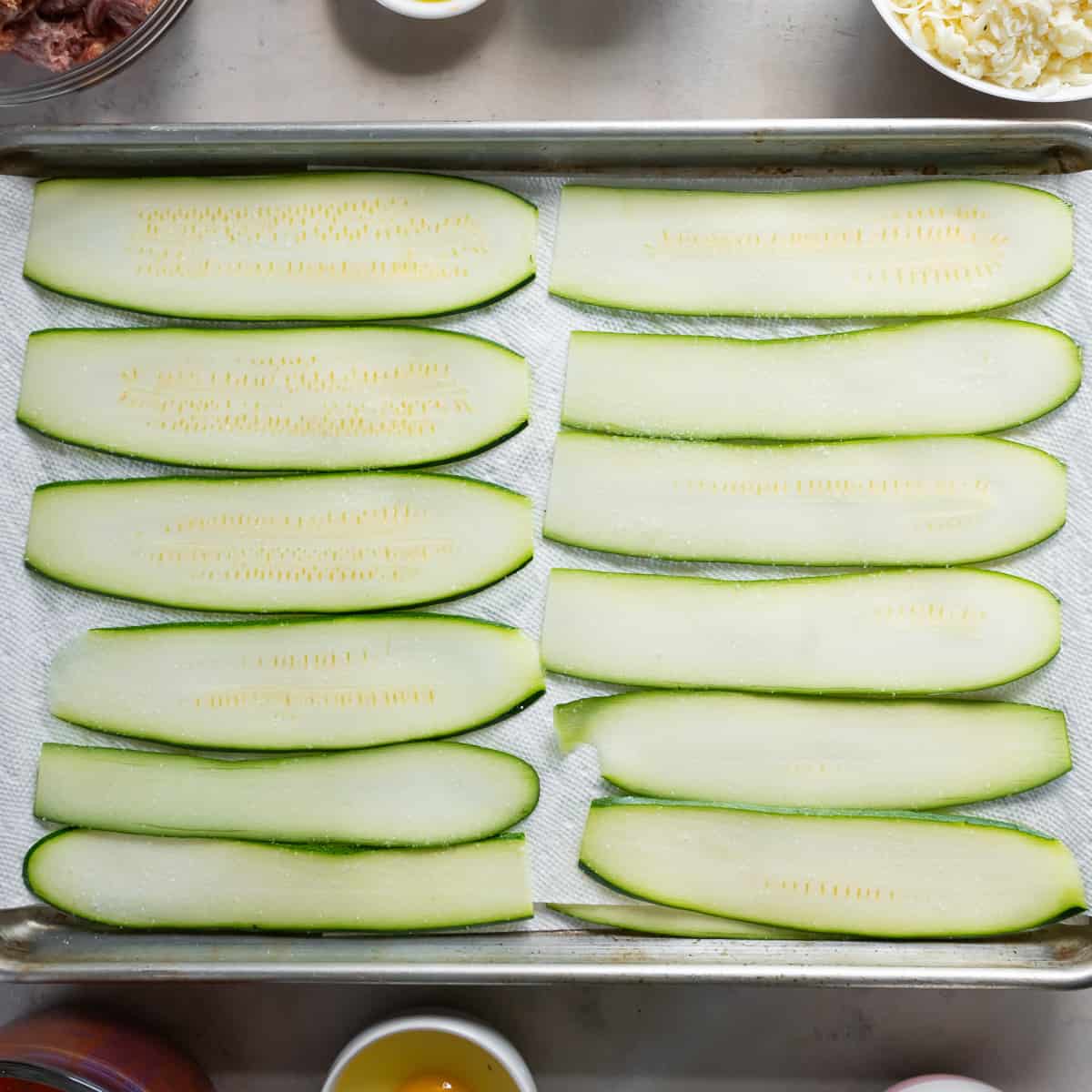 Sliced zucchini on a paper towel lined baking sheet.