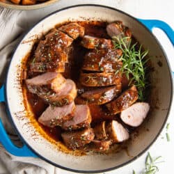A top down shot of sliced Apricot Glazed Pork Tenderloin in a blue skillet with sprigs of fresh rosemary.