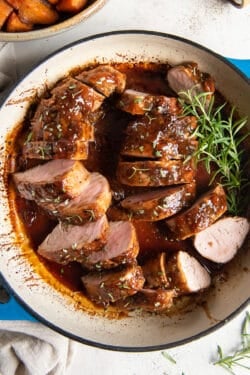 A top down shot of slices of Apricot Glazed Pork Tenderloin in a pan with sprigs of fresh rosemary.