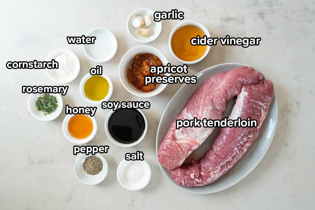 The ingredients for Apricot Glazed Pork Tenderloin on a white surface with text.