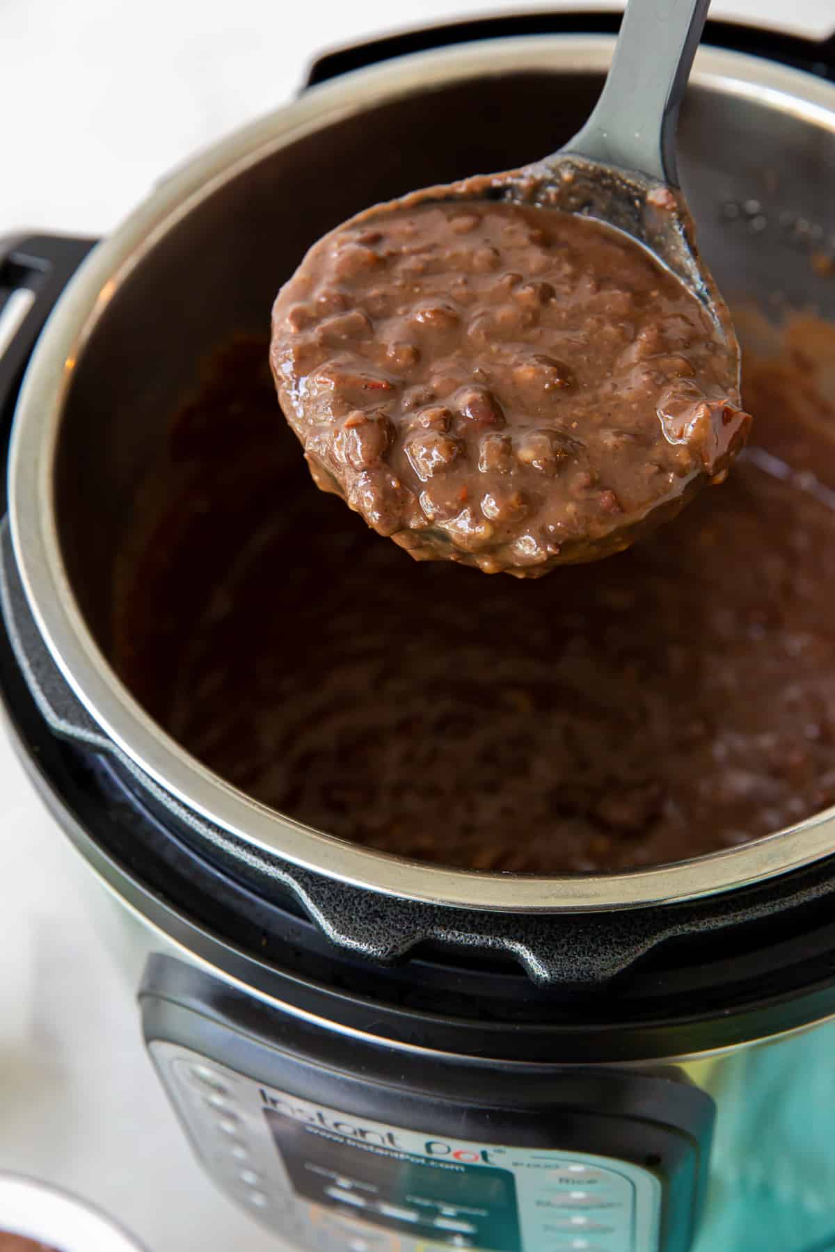 A ladle full of black bean soup hovering over an Instant Pot.
