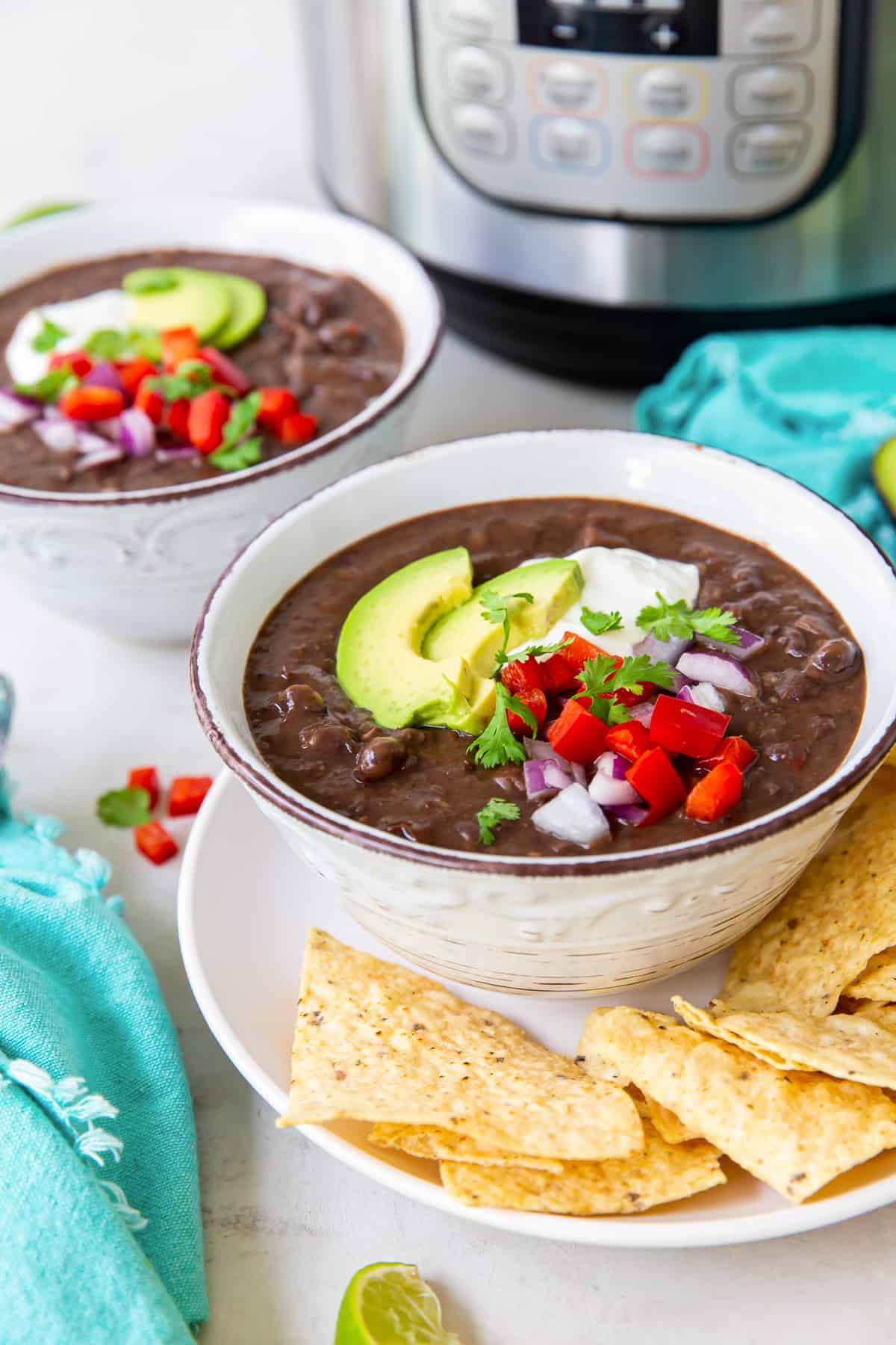 Two bowls of black bean soup topped with avocado and sour cream in front of an Instant Pot.