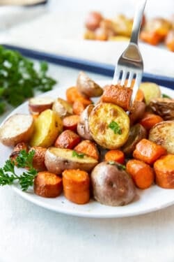 A fork piercing a potato and carrot on a plate filled with roasted vegetables.