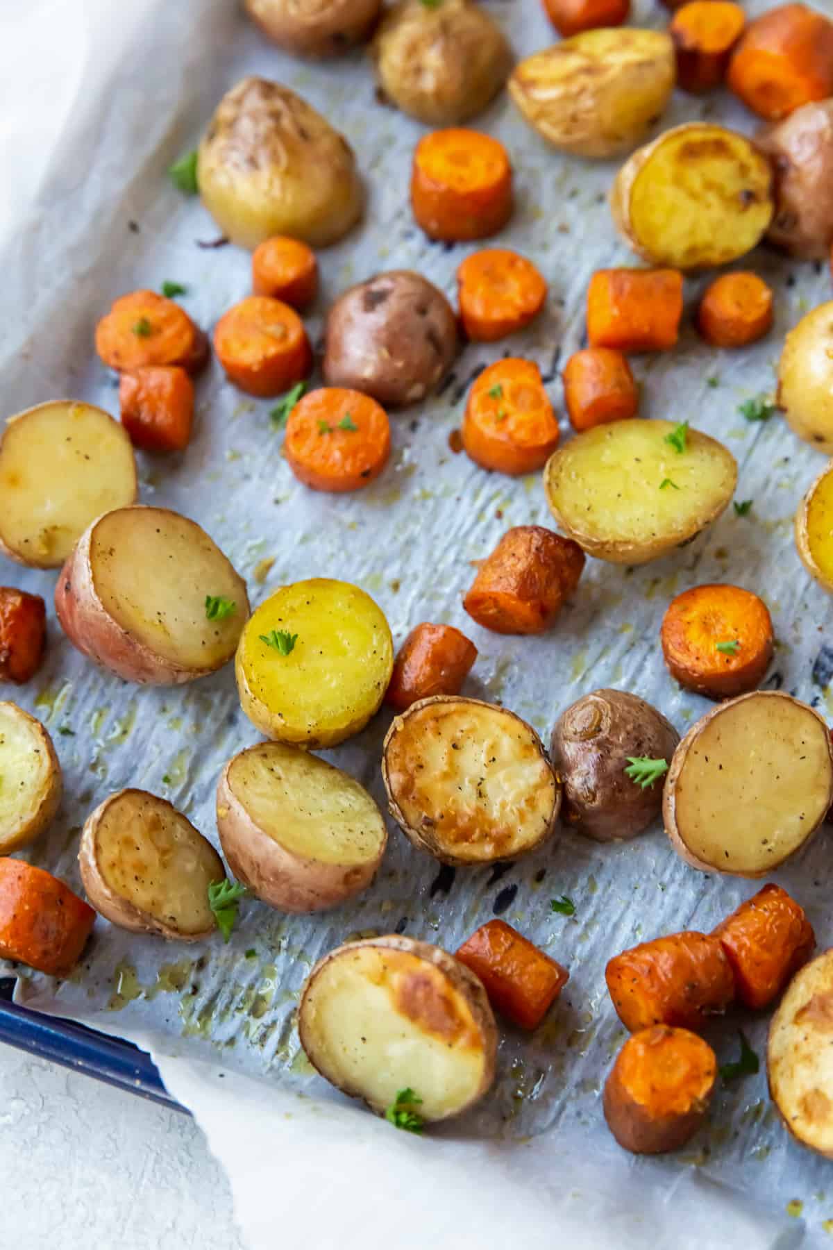 A close up of chunks of roasted carrots and potatoes on a parchment paper lined baking sheet.